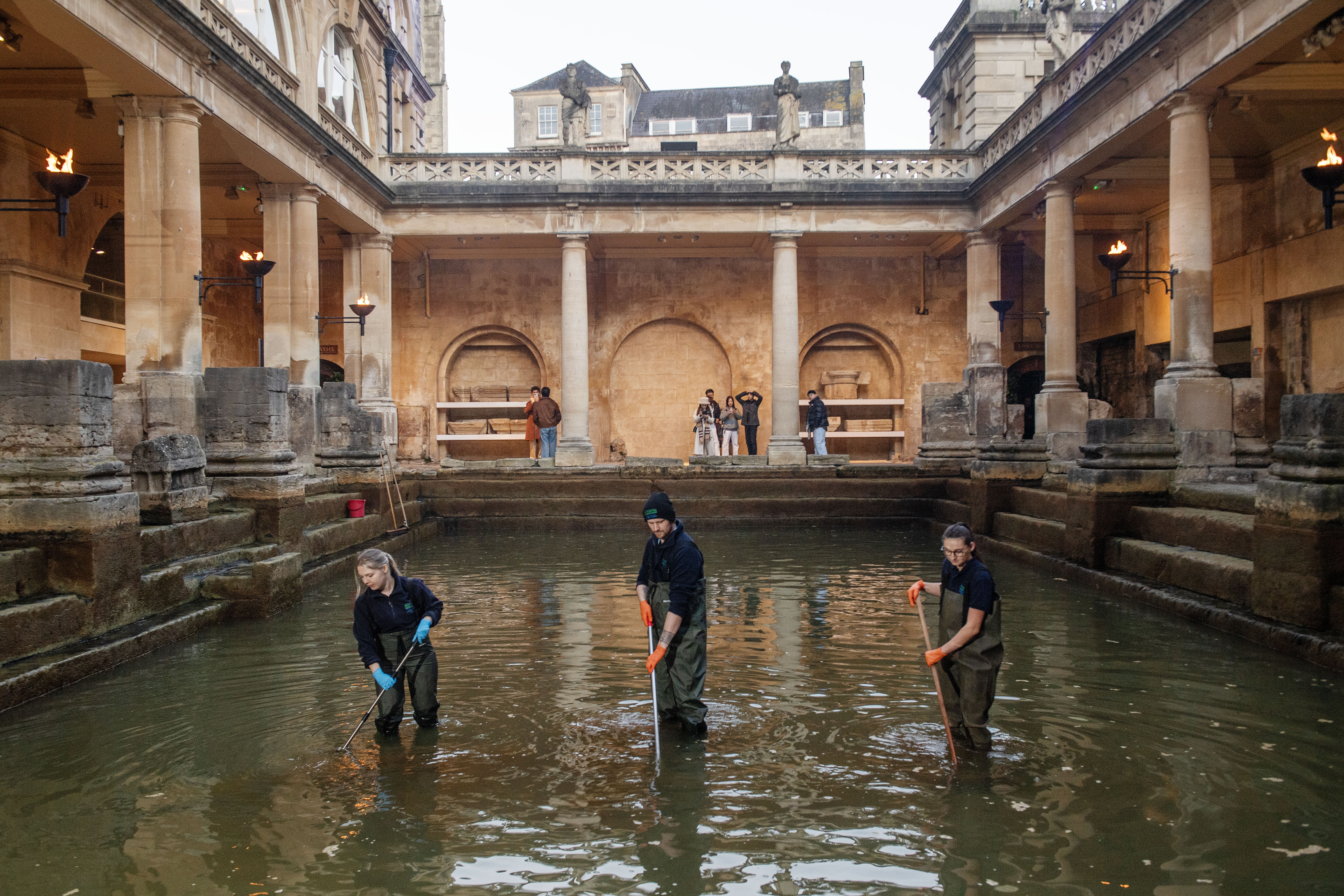 Image: Three members of the Operations team are standing in the Great Bath with brushes