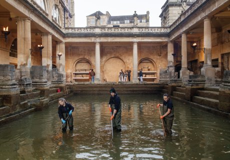 Image: Three members of the Operations team are standing in the Great Bath with brushes