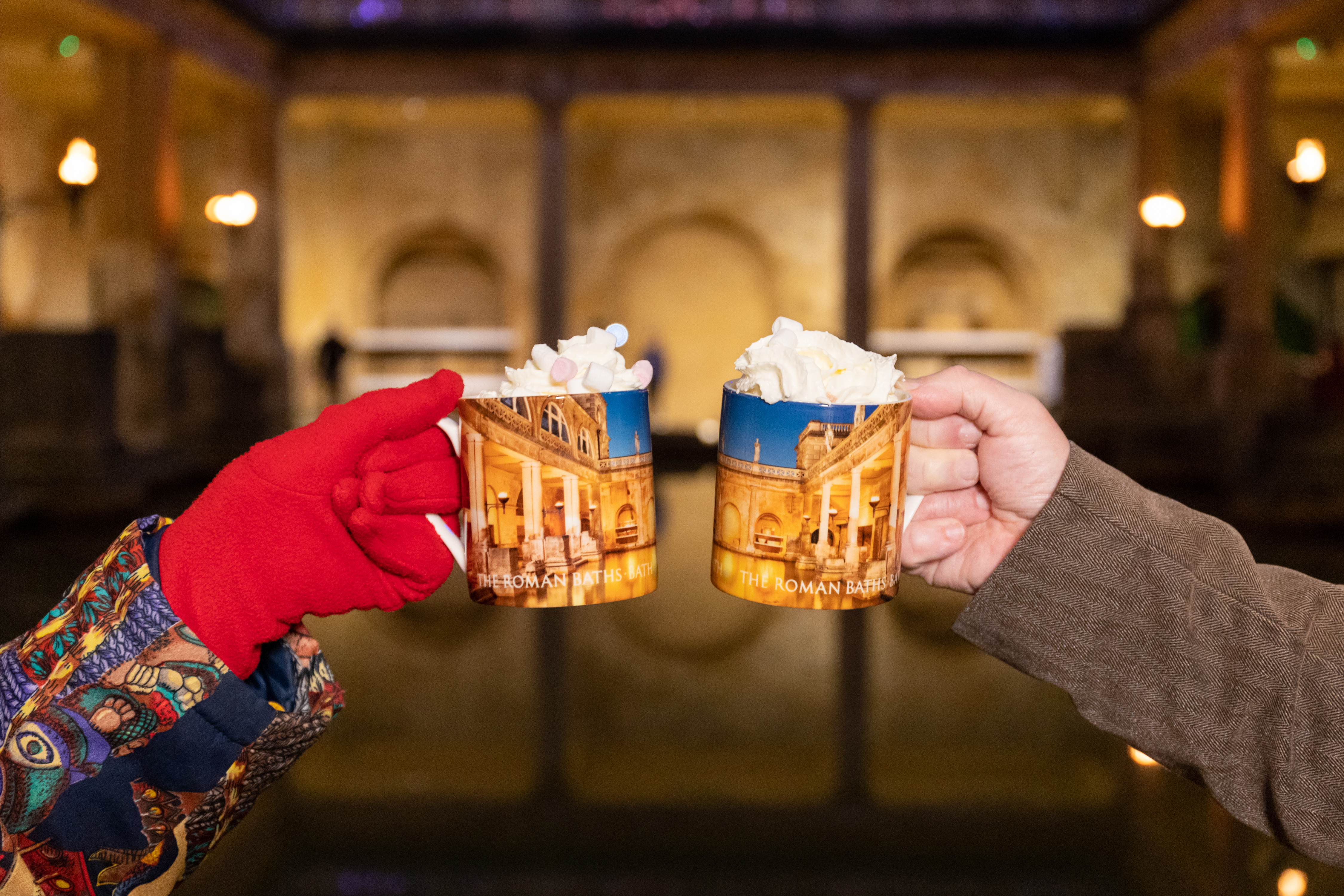 Image: Two people holding mugs of hot chocolate beside the Great Bath