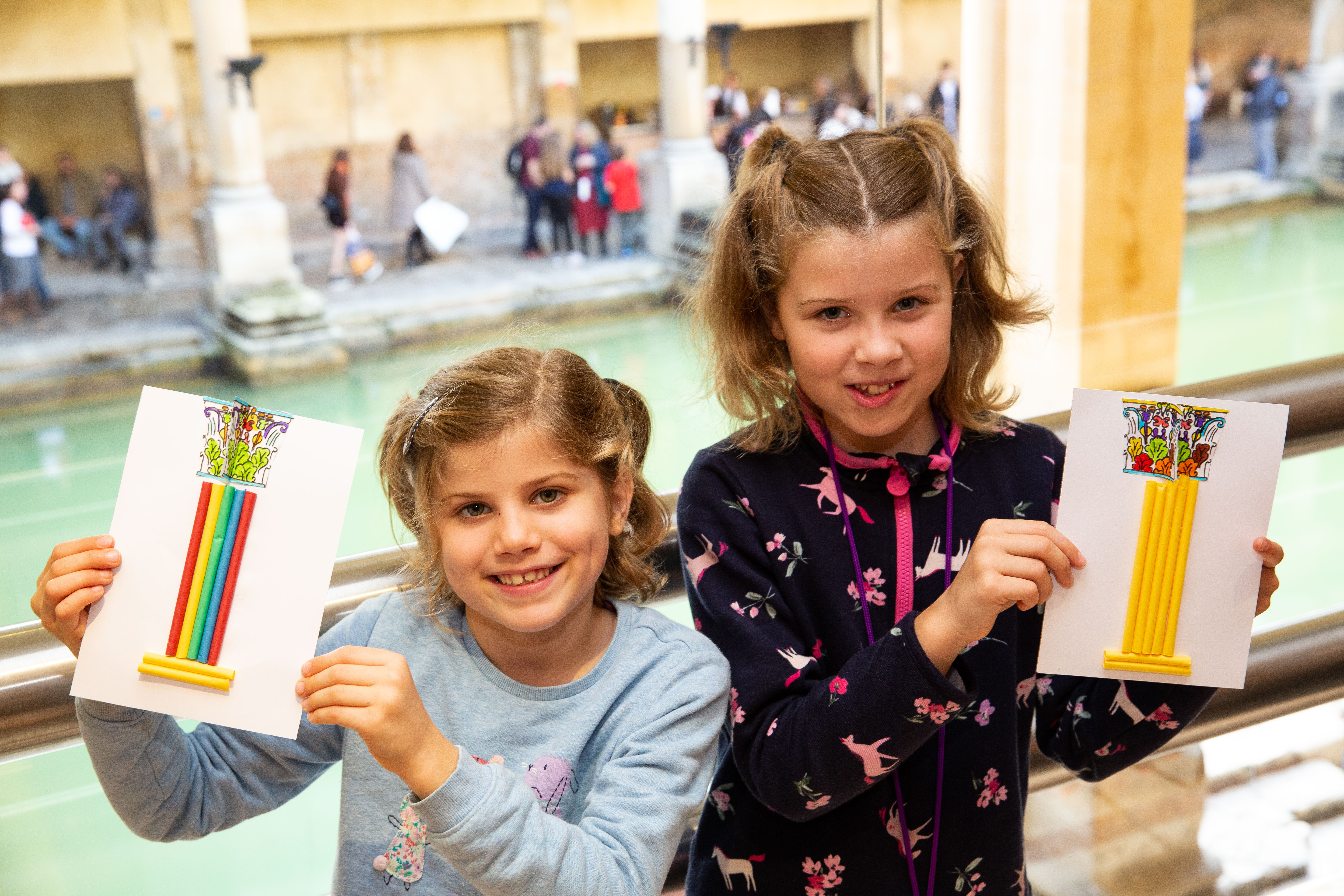 Two girls showing off their artworks made from straws and felt tips