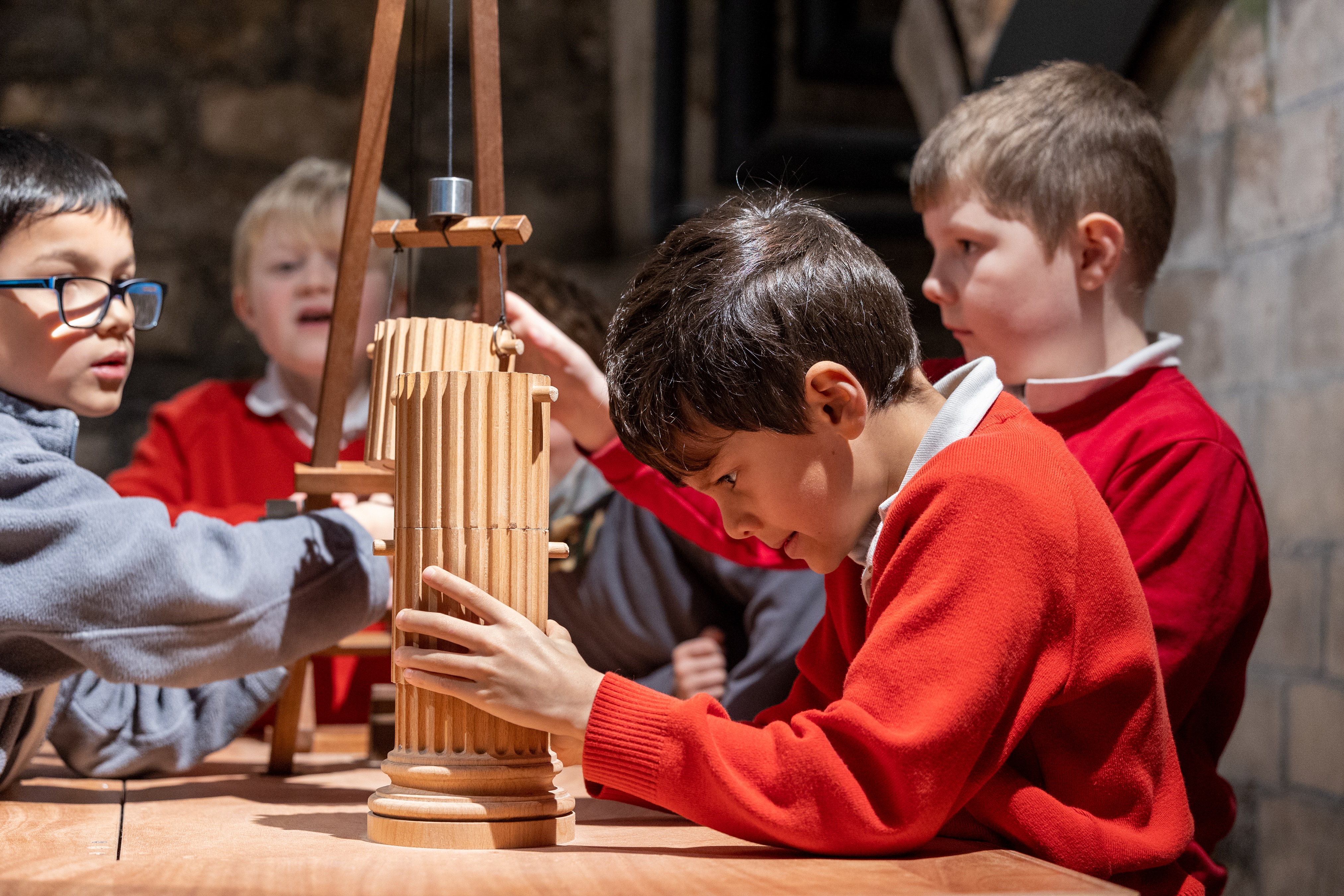 Four school boys using a model crane to build a wooden column