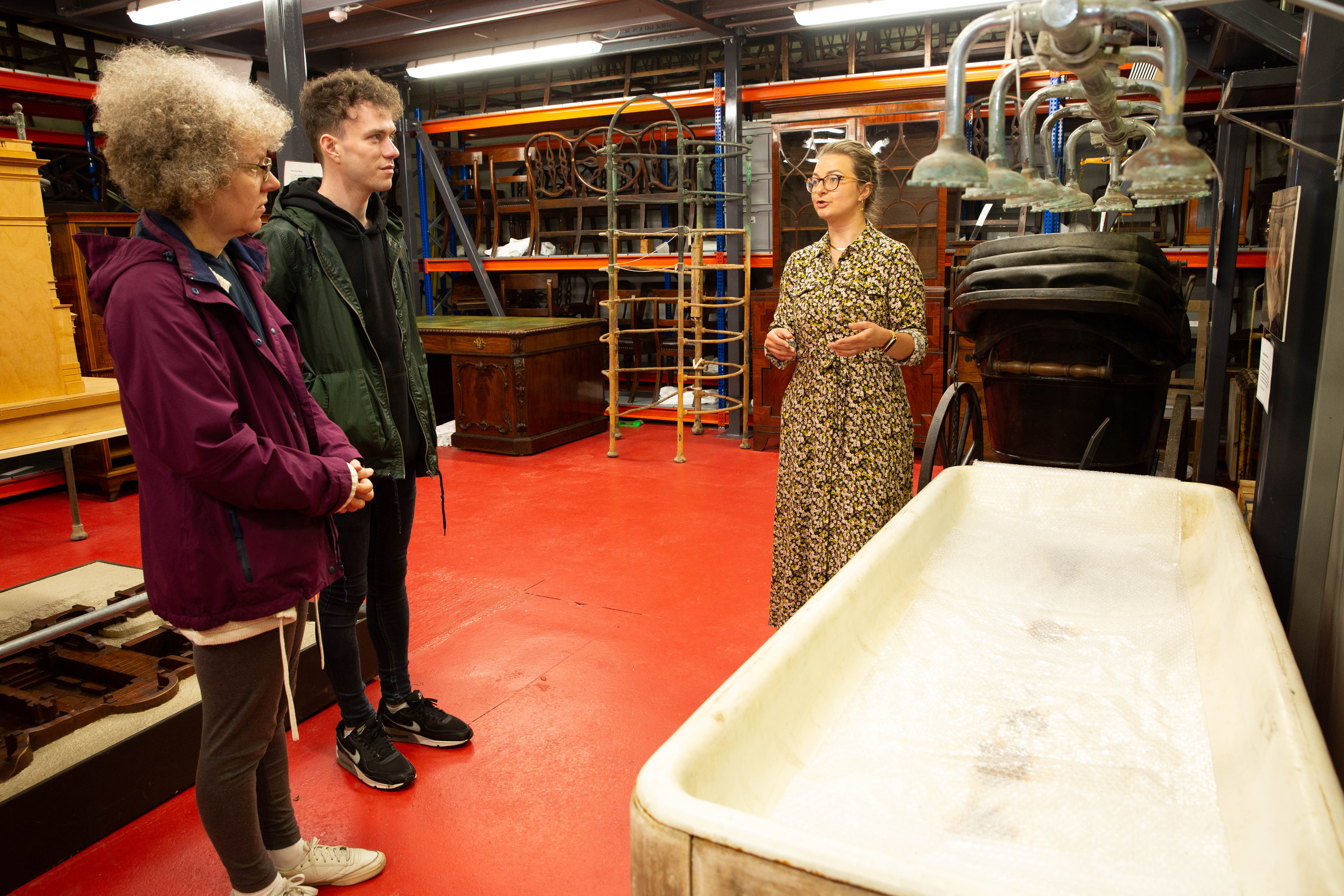 Two people on a store tour with a curator, looking at an old fashioned shower