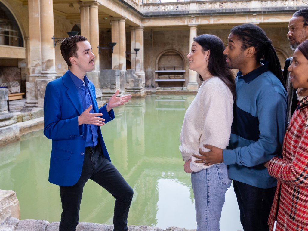 A group listen to a tour of the Great Bath