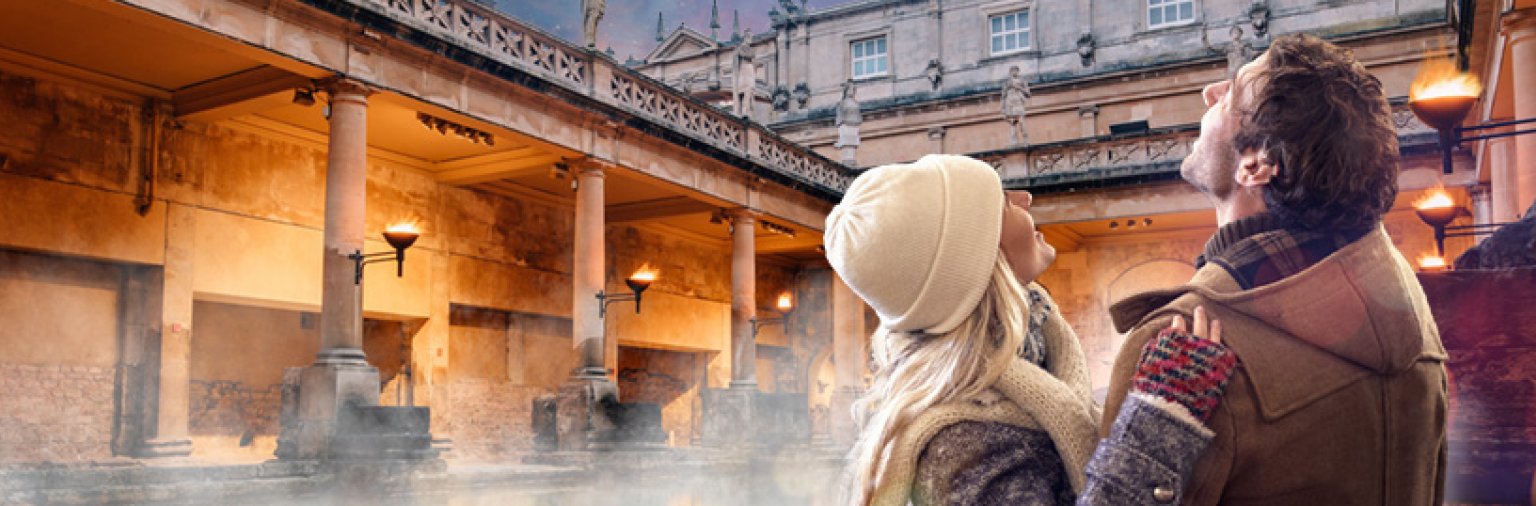 Share the magic at The Roman Baths this winter. A couple enjoy the Great Bath by torchlight.