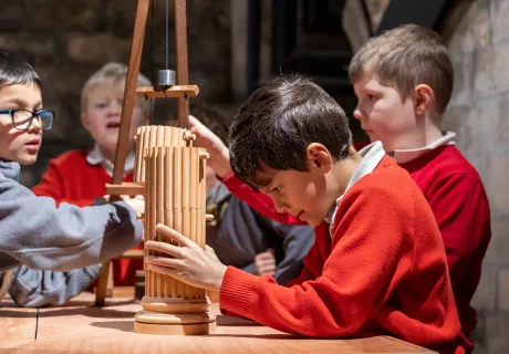 Four school boys using a model crane to build a wooden column