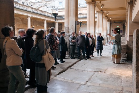 A group of people standing watching a performance by the Great Bath